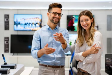 Tüketici elektroniği mağazasında yeni dijital cihaza bakan mutlu gençler