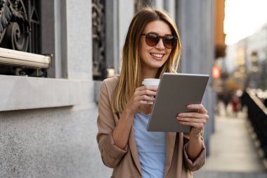 Çekici genç ve başarılı kadın kahve içiyor ve tatilin tadını çıkarırken dijital tablet kullanıyor.