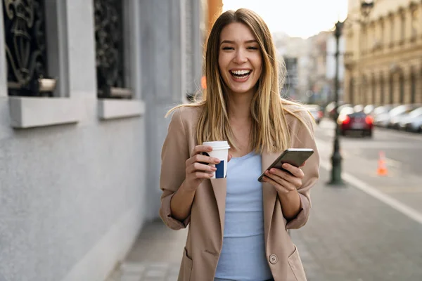 Beautiful young success woman with coffee using mobile phone against urban city background. People business break device concept