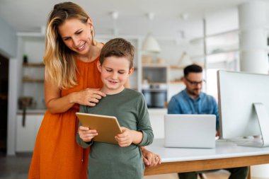 Uzaktan öğrenme, online eğitim, ev işi okulu konsepti. Evde dijital cihazları olan mutlu bir aile.