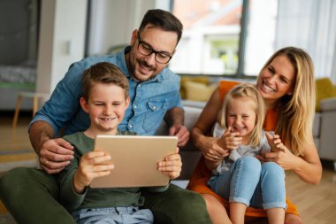Mutlu genç aile evde eğleniyor. Çocuklu aileler dijital cihaz kullanıyor. Eğitim ebeveynliği mutluluk kavramı.