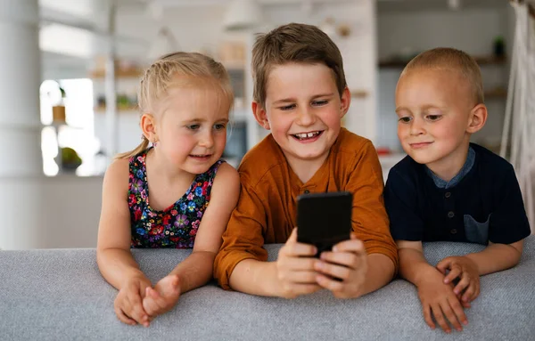 Portrait of children having fun, playing on mobile phone together at home. Internet and network addiction.