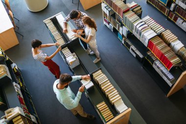 Kütüphanede kitaplarla çalışan mutlu genç üniversite öğrencileri. Üniversitede bir grup çok ırklı insan