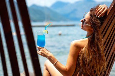Bikini giyen, yaz tatilinde kokteyl içen mutlu genç bir kadın. İnsanlar eğlence konseptiyle seyahat eder.
