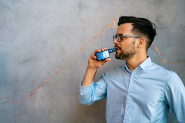 Sigara ve vapur kullanmak sağlıksız ve bağımlılık yapıcı olabilir ve akciğerler için sağlık riski oluşturabilir. Elektronik sigara kullanan bir adam..