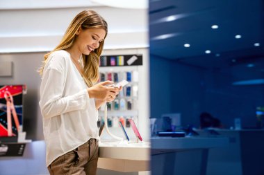 Alet dükkanından akıllı telefon alan mutlu genç bir kadının portresi. Yeni bir dijital aygıt alınıyor