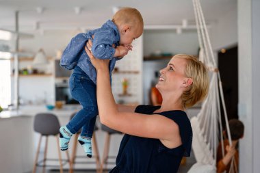İçeride mutlu bir uyum içinde bir aile. Güzel anne portresi ve tatlı bebek birlikte gülüşerek oynuyorlar..