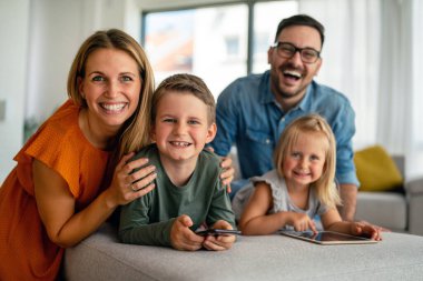 Mutlu genç aile evde eğleniyor. Çocuklu aileler dijital cihaz kullanıyor. Eğitim ebeveynliği mutluluk kavramı.
