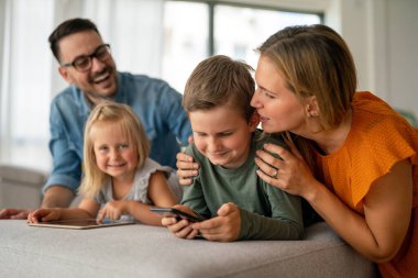 Mutlu genç aile evde eğleniyor. Çocuklu aileler dijital cihaz kullanıyor. Eğitim ebeveynliği mutluluk kavramı.