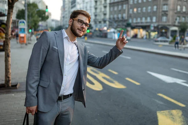 Man calling a taxi. Concept about urban life, people and transportation. Young smiling business man catching taxi at city street. Man looking for a taxi