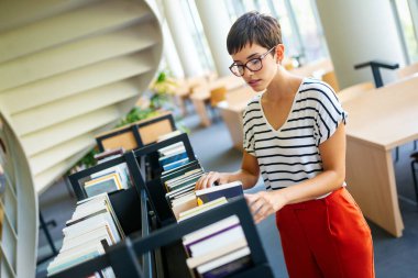 Eğitim kütüphanesi, üniversite eğitimi ve insanların konsepti. Üniversite kütüphanesinde kitap okuyan gülümseyen öğrenci kız.