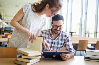 Eğitim kampüsü arkadaşlığı ve insanların konsepti. Bir grup mutlu öğrenci kütüphanede birlikte okuyorlar..