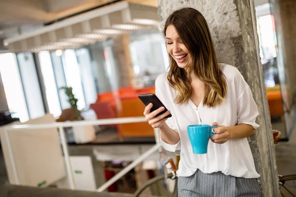 Portrait of a happy young success woman using smartphone and drinking coffee in break in office. Business people success social network concept