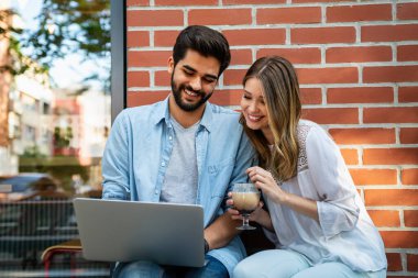 Kafede oturmuş gülümseyen, dizüstü bilgisayara bakan, keyifle vakit geçiren, kahve içen mutlu genç bir çift..
