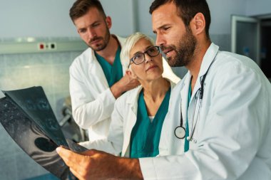 Bir grup doktor hastanedeki röntgenlere bakarak hastanın teşhisini tartışıyor.