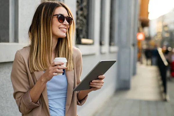 Beautiful young success woman with coffee using digital tablet against urban city background. People business break device concept