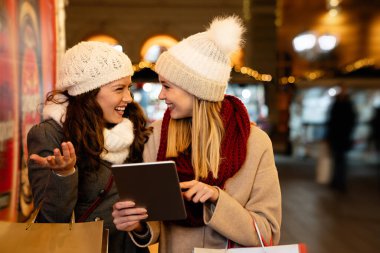 İnsanlar Noel alışverişinde dijital tablet konsepti alıyorlar. Mutlu kadın arkadaşlar birlikte dışarıda alışveriş yapıyorlar..