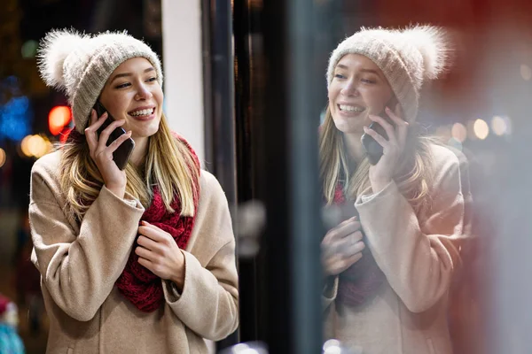 Young beautiful woman using her mobile phone surfing the net with smartphone on a winter day in the street. People technology happiness concept