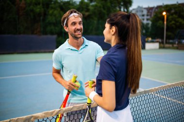 Tenis sporu insanları konsepti. Karışık genç çiftler oyuncusu tenis topuna vuruyor ve partner kalenin yanında duruyor