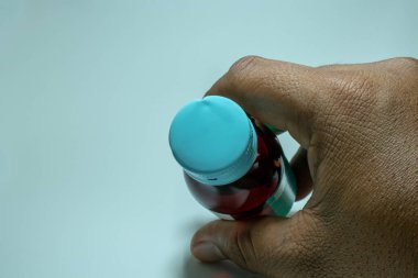 Beyaz arka planda bir şişe parasetamol şurubu tutan bir el..