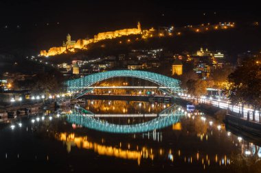 Tiflis, Gürcistan - 4 Aralık 2021: Narikala Kalesi ve Kura Nehri üzerinde aydınlatılmış Barış Köprüsü. Seyahat