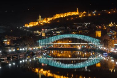 Tiflis, Gürcistan - 4 Aralık 2021: Narikala Kalesi ve Kura Nehri üzerinde aydınlatılmış Barış Köprüsü. Seyahat