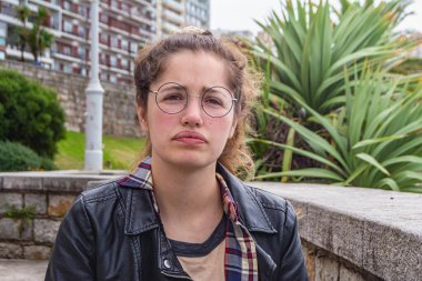 Deri ceketli ciddi sarışın kadın yan bakıyor.