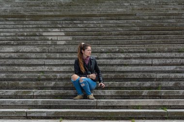 Taş merdivenlerde deri ceketli bir kadın.