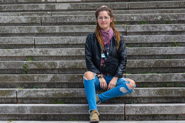 Taş merdivenlerde deri ceketli bir kadın.