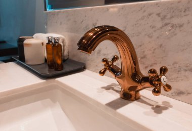 Beyaz granit lavabonun üzerindeki temiz ve yeni altın renkli musluk otel odasında.