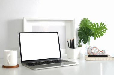Computer laptop with blank display, pencil holder, coffee cup and houseplant on white table.	