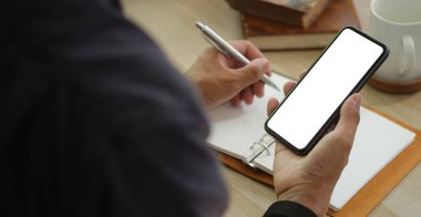 Kesilen adam akıllı telefon tutuyor ve not defterine not alıyor..