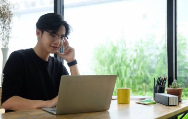 Ofiste bilgisayarla çalışan gülümseyen Asyalı adam..