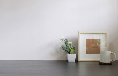 Ev bitkisi, kamera ve kahve fincanı ile beyaz masa ve tuğla duvarlı şık çalışma alanı.