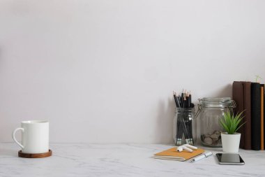 Ev bitkisi, kamera ve kahve fincanı ile beyaz masa ve tuğla duvarlı şık çalışma alanı.