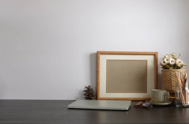 Ev bitkisi, kamera ve kahve fincanı ile beyaz masa ve tuğla duvarlı şık çalışma alanı.