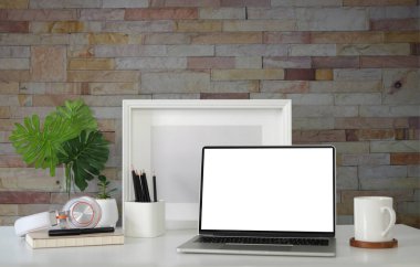 Front view creative workplace with computer laptop, coffee cup and picture frame on white table with brick wall.	