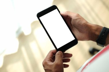 Genç adam oturma odasında oturuyor ve akıllı telefon kullanıyor..