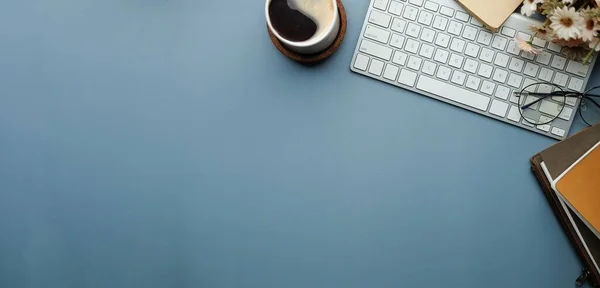 Kablosuz klavye, kahve fincanı ve mavi arkaplanda not defteri.