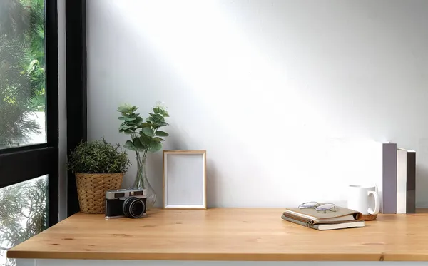 Creative workspace with blank poster frame, camera, coffee cup and houseplant on wood table.	