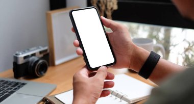 Genç adam ofiste oturuyor ve akıllı telefon kullanıyor..