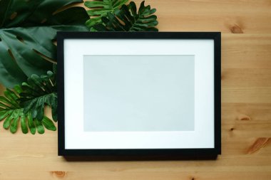 Boş fotoğraf çerçevesi ve ahşap arkaplanda yeşil yapraklar.