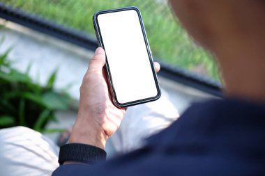 Bahçede otururken akıllı telefon kullanan genç adamın omuzlarının üstünden..