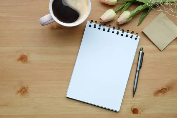 Not defteri, yapışkan not, kahve fincanı ve ahşap arka planda pembe laleler..