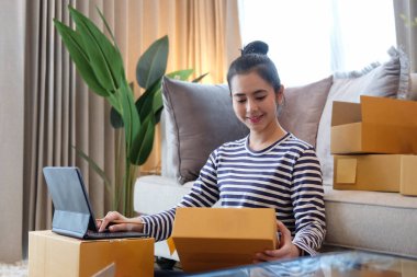 Gülümseyen Asyalı kadın çevrimiçi satıcı müşteriye teslimat için paket kutuları hazırlıyor. Çevrimiçi veya e-ticaret konsepti satılıyor.