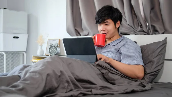 Uśmiechnięty Przystojniak Pijący Kawę Korzystający Laptopa Łóżku — Zdjęcie stockowe