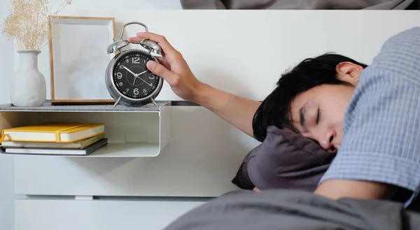 stock image Sleepy man lying on bed and turning off alarm clock switch in the morning.