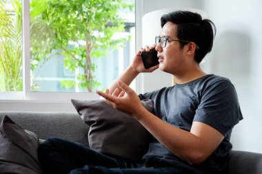 Young man sitting in living room and talking on smart phone.	
