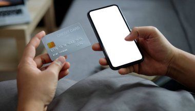 Smiling young man holding credit card and making banking online or shopping online on smart phone.	
