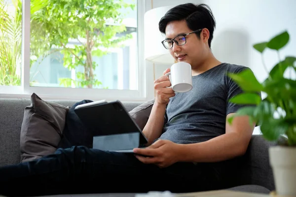 Young Asian Man Sitting Comfortable Sofa Using Digital Tablet — стокове фото